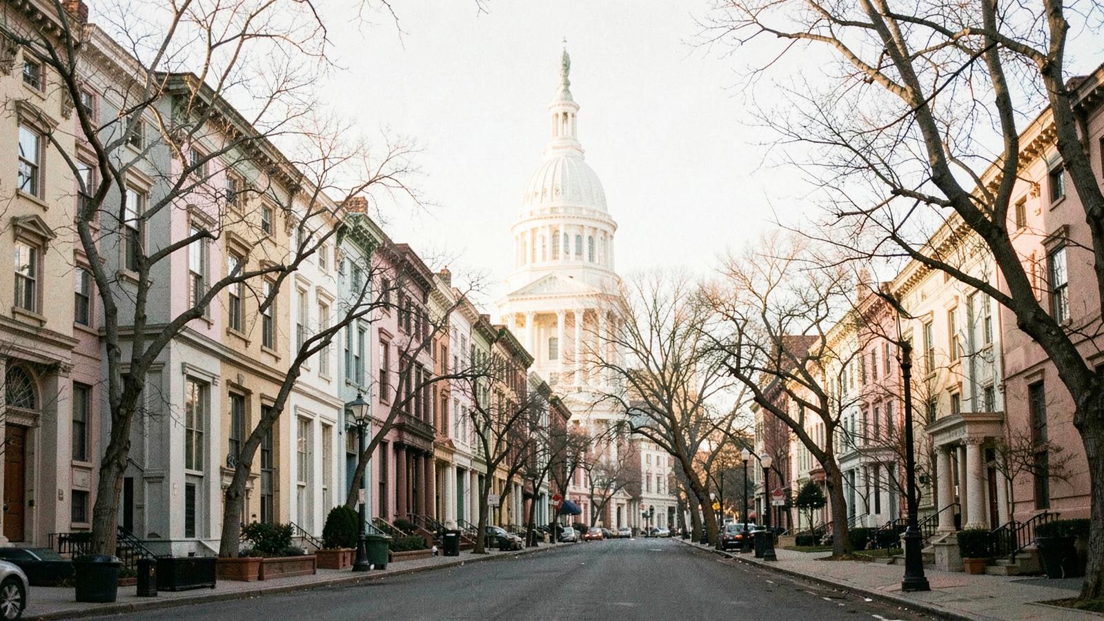A Capitol Hill residential street of pastel rowhouses at dawn, the dome visible at the end of the block