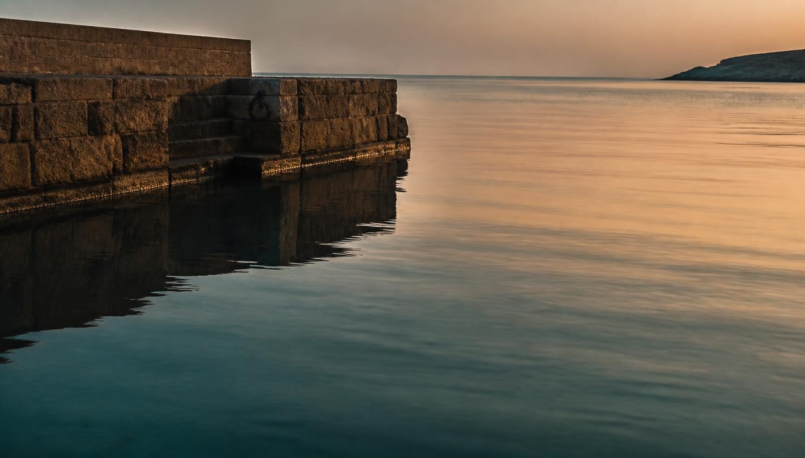 Still water at a quiet harbour wall at dusk