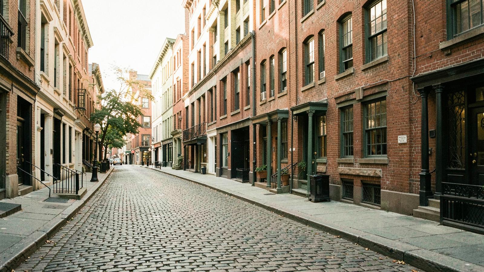 A cobblestone Georgetown side street in Washington, D.C., historic brick facades in low sunlight